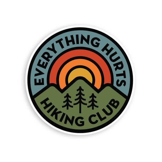 Round Everything Hurts Hiking Club sticker with a sunset arch, green mountains and three pines on white.
