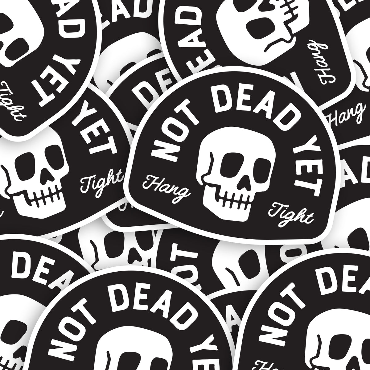 A scattered pile of Not Dead Yet stickers shows the skull design repeated at different angles.