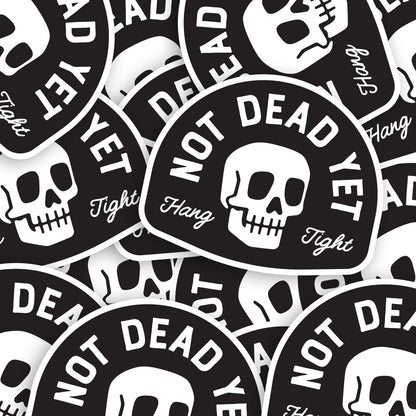 A scattered pile of Not Dead Yet stickers shows the skull design repeated at different angles.