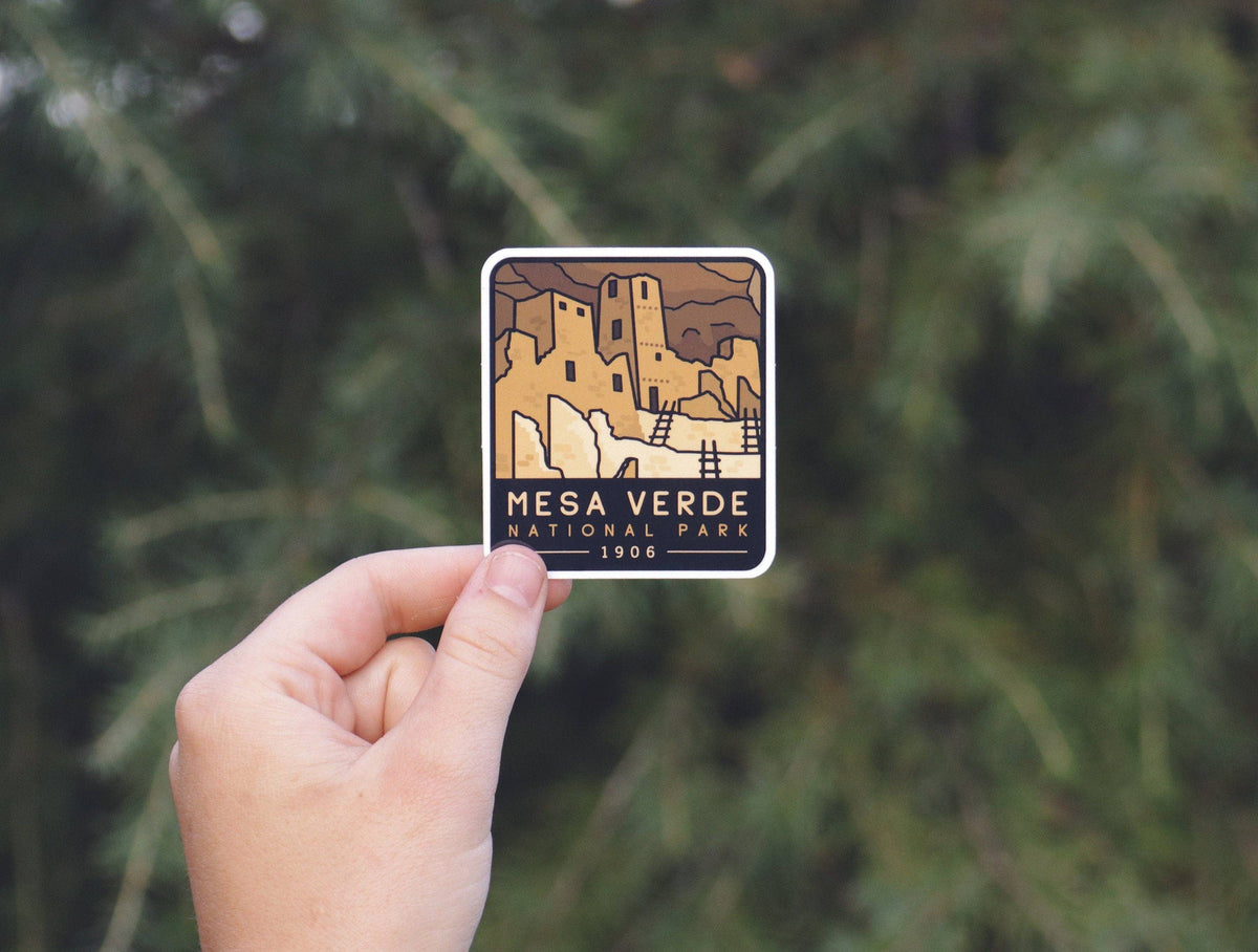 Held higher than the rest, the Mesa Verde National Park sticker shows cliff dwellings and ladders.