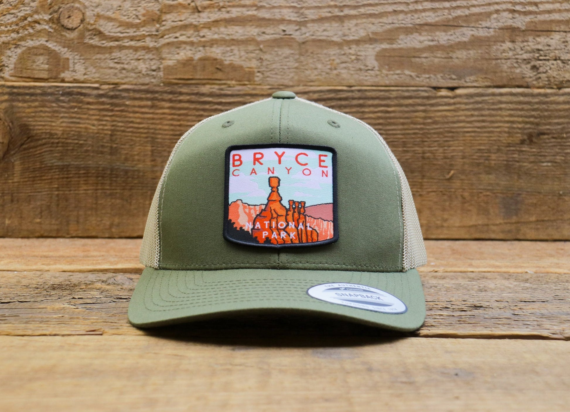 Straight on before barn boards, the Bryce Canyon National Park trucker hat centers its hoodoo and red lettering patch.