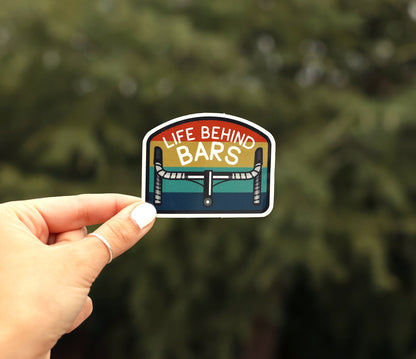 Held further from the camera, the Life Behind Bars sticker shows its striped arch and drop handlebars outdoors.