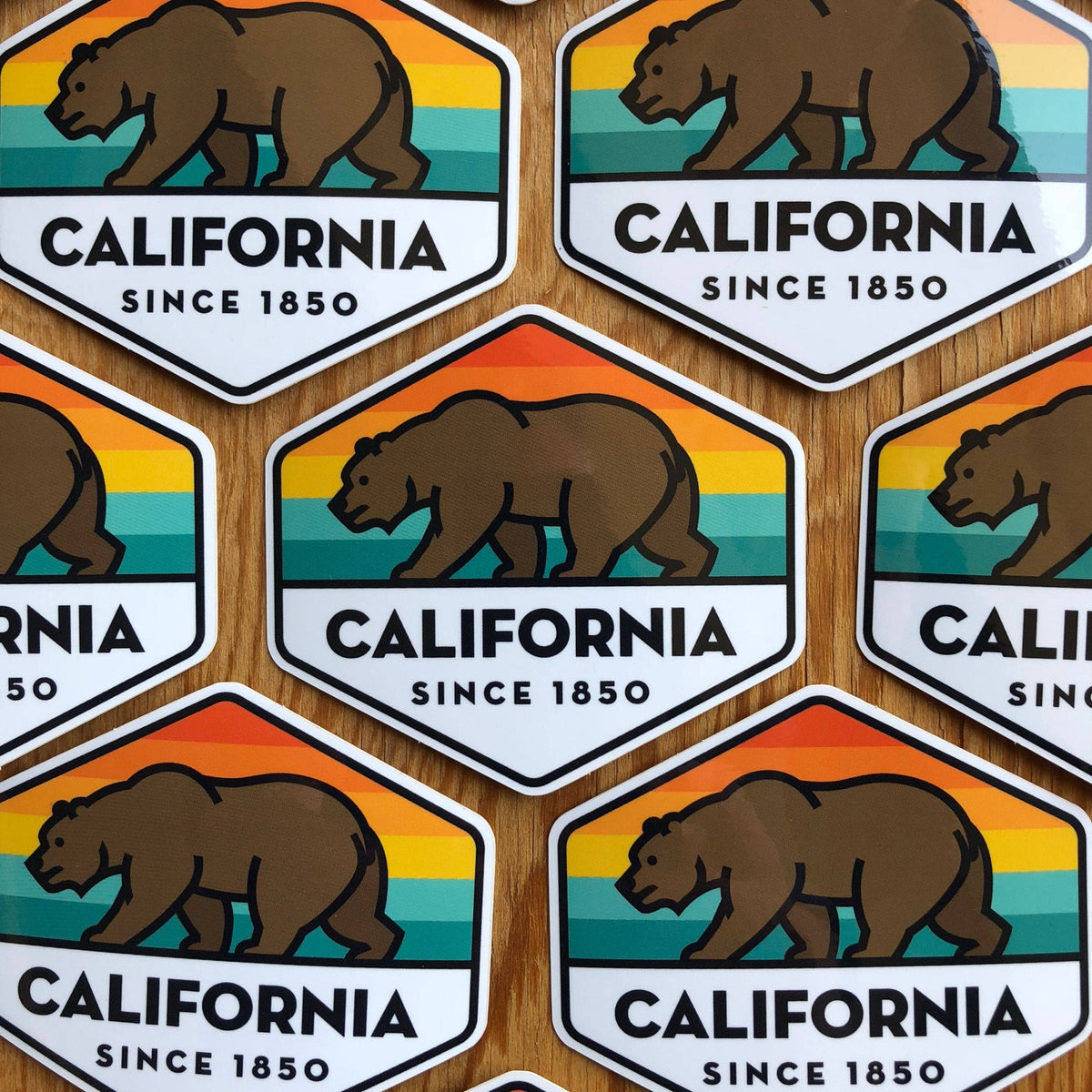 Overlapping rows of California State Bear stickers cover a wooden tabletop.