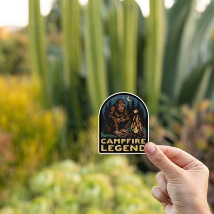 Tall cactus and succulents fill the background as fingers hold the Campfire Legend sticker at golden hour.