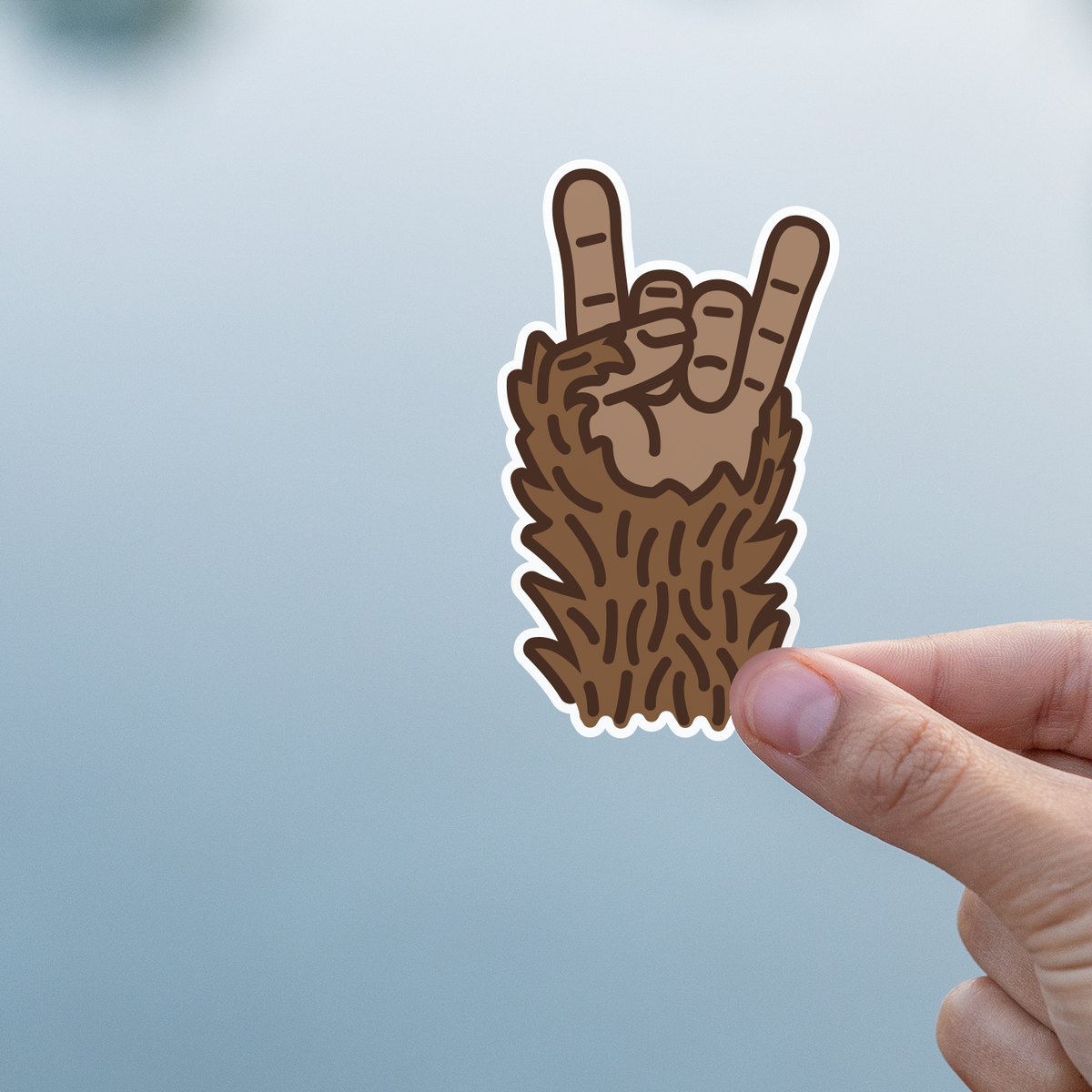 Held by finger and thumb, the Bigfoot Rocks sticker reads clearly against a soft blue grey background.