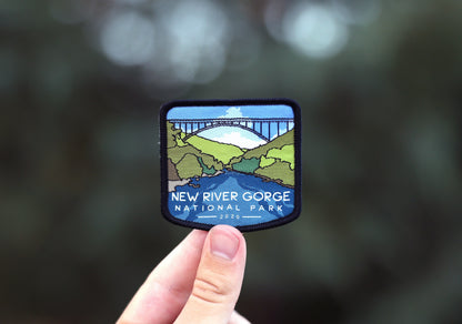 Held at fingertip height, the New River Gorge patch stands against soft bokeh from the woods behind it.