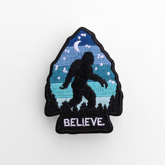 On plain white, the arrowhead shaped Bigfoot Believe patch stitches a dark sasquatch under a blue night sky.
