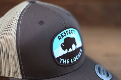 Close crop on the brown trucker hat, where the Respect The Locals patch curves over the front panel.