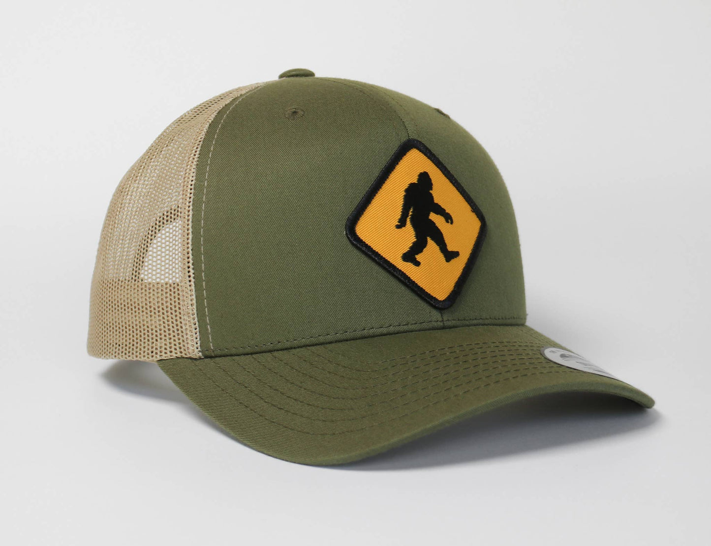 Olive front and khaki mesh on the Bigfoot Crossing trucker hat, with the yellow diamond patch on the crown.