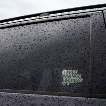 Applied to the rain beaded window of a dark car, the Free Range Mama sticker sits near the door frame.