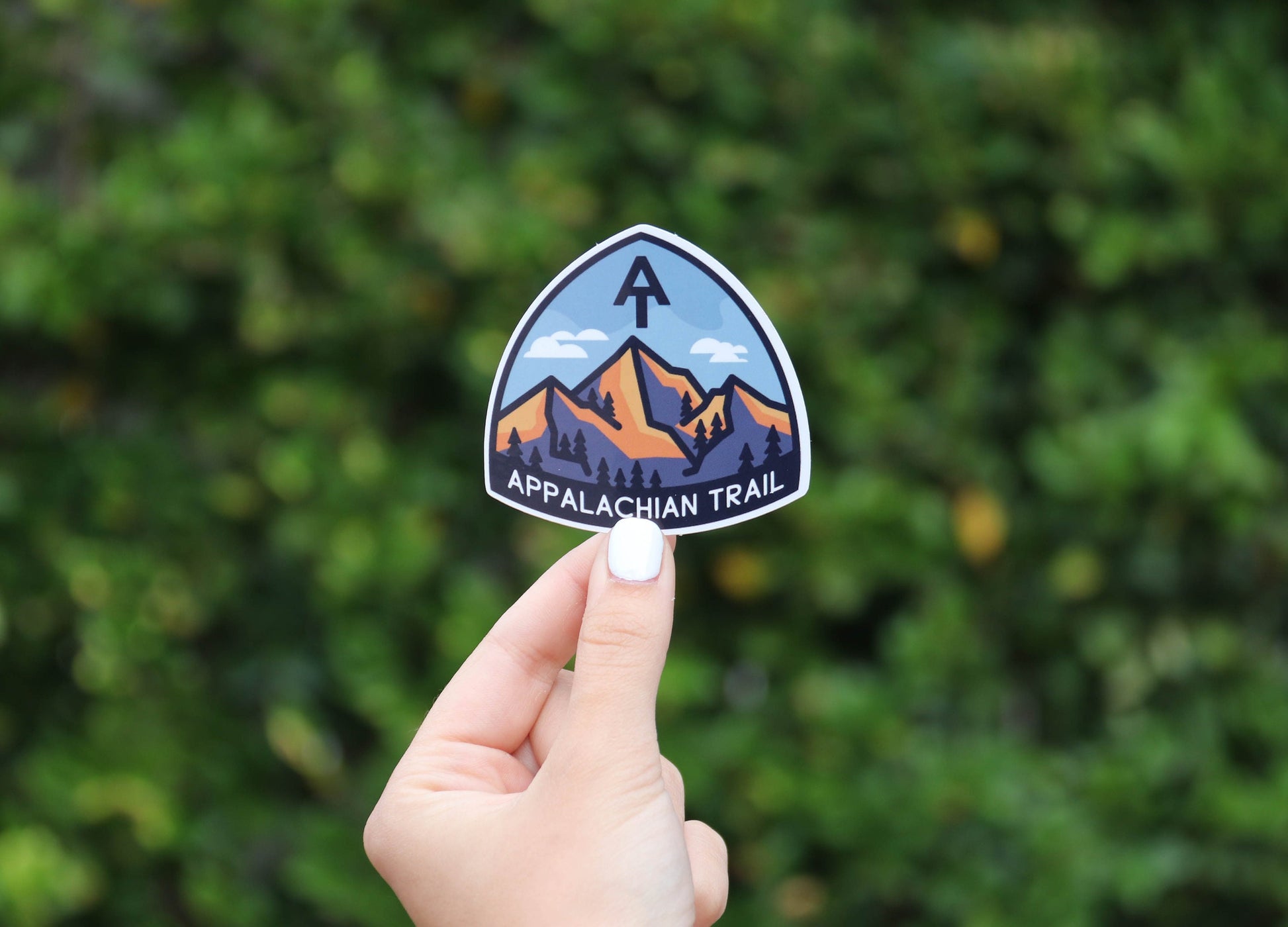 Pulled back farther, the same Appalachian Trail sticker sits small between two fingers against the hedge.