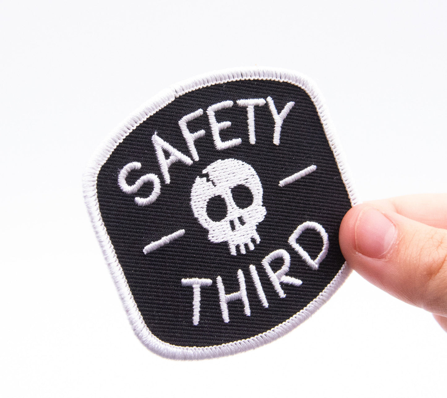 A thumb steadies the Safety Third patch at its corner, filling the frame against clean white.