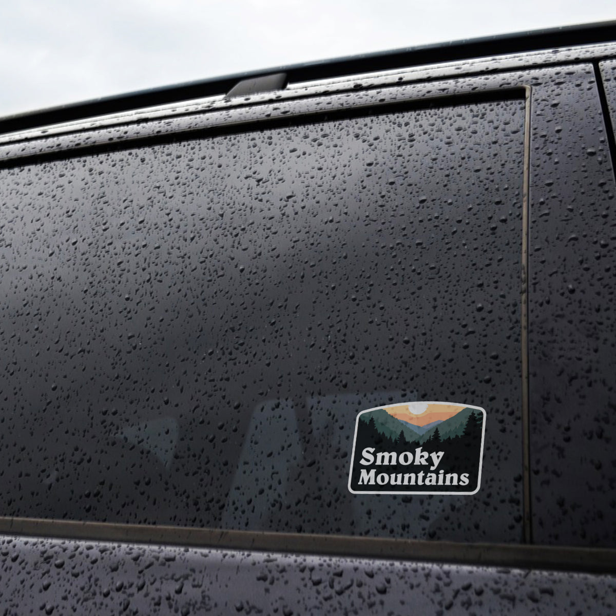 Rain beads across a dark truck window where the Smoky Mountains sticker sits near the lower corner.