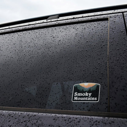 Rain beads across a dark truck window where the Smoky Mountains sticker sits near the lower corner.