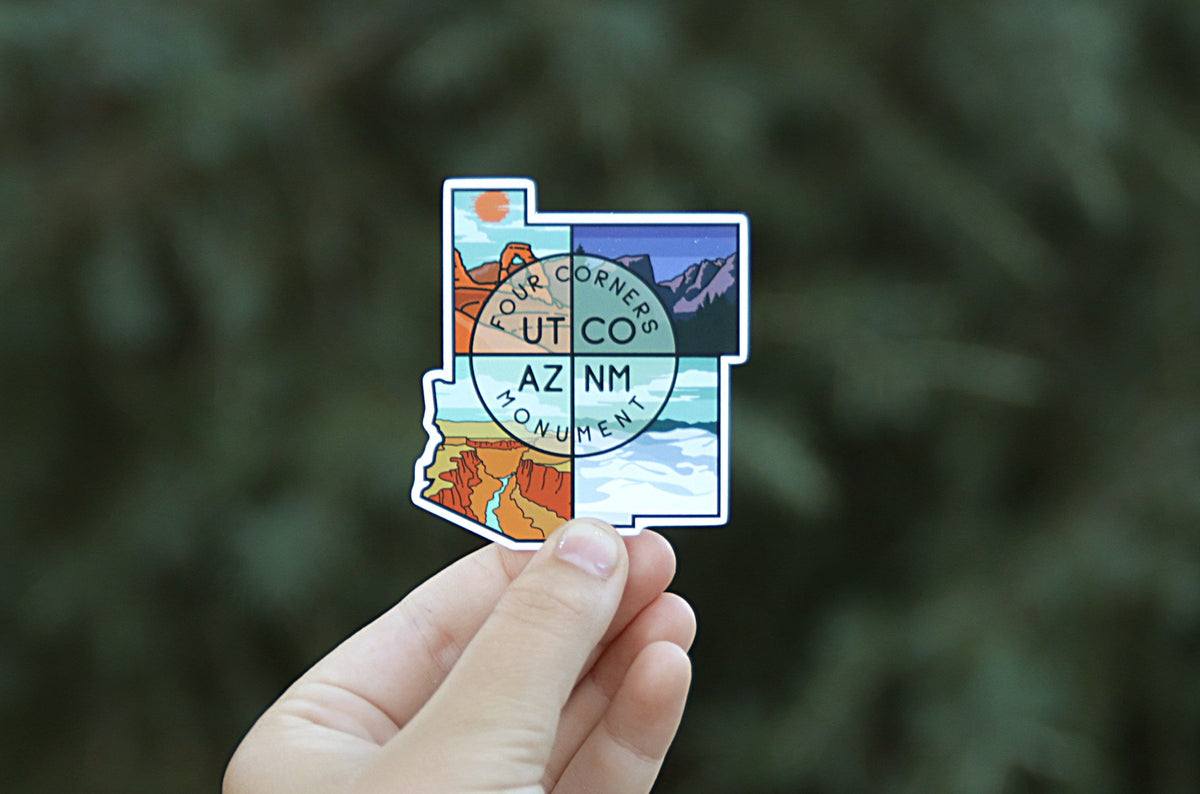 Held further back against blurred green branches, the Four Corners Monument sticker shows its full state outline shape.