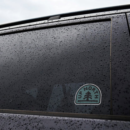 Rain beads on a dark car window where the Up North sticker rests near the lower corner.