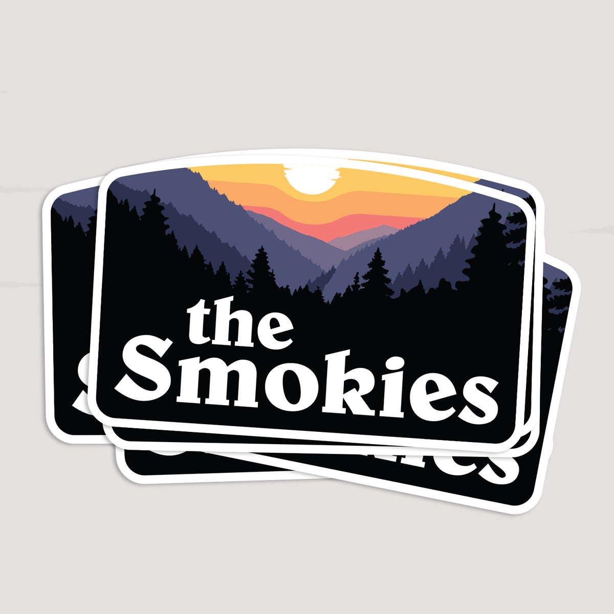 Three The Smokies stickers fan out in a stack, each showing the same sunset mountain scene.