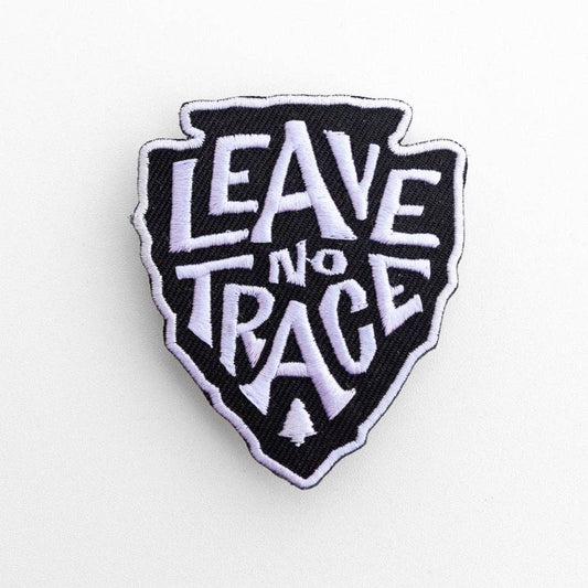 Arrowhead shaped Leave No Trace patch on white, its white lettering and small pine tree stitched over black.