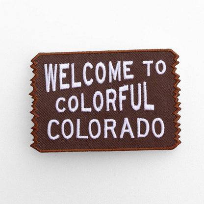 Flat on white, the brown Welcome to Colorful Colorado patch shows white lettering and a zigzag border.