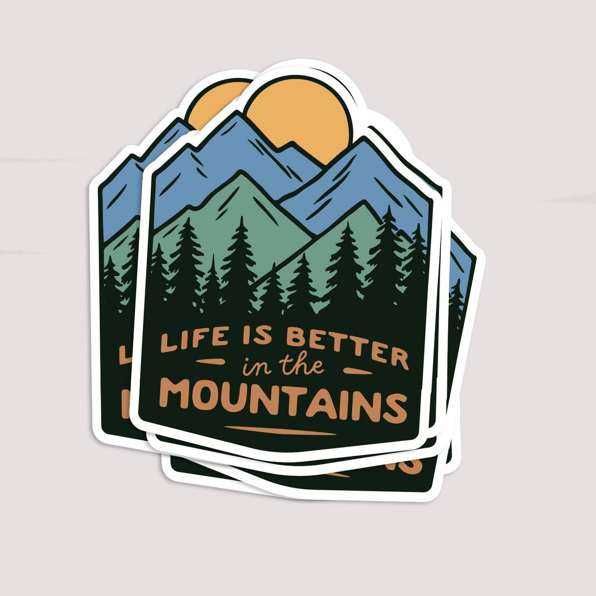 Three Life Is Better In The Mountains stickers fanned in a stack on a pale grey backdrop.