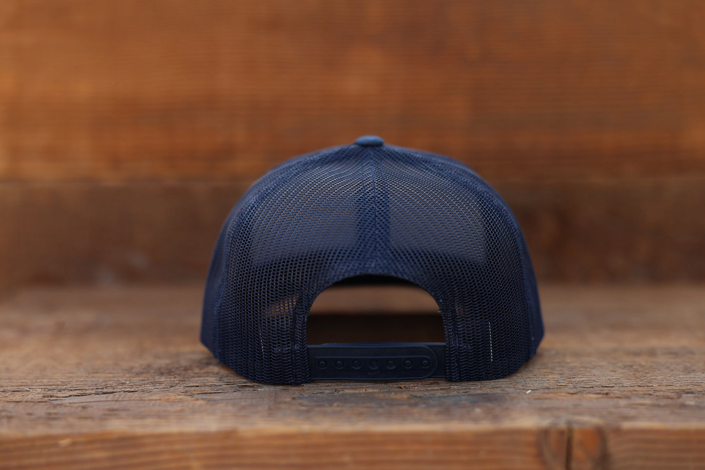 Rear view against barn wood, the navy Olympic National Park trucker hat closes with a plastic snap strap.