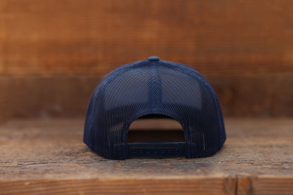 Rear view against barn wood, the navy Olympic National Park trucker hat closes with a plastic snap strap.