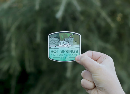 Pulled back a little, the Hot Springs National Park sticker sits small in the frame against a soft green conifer.