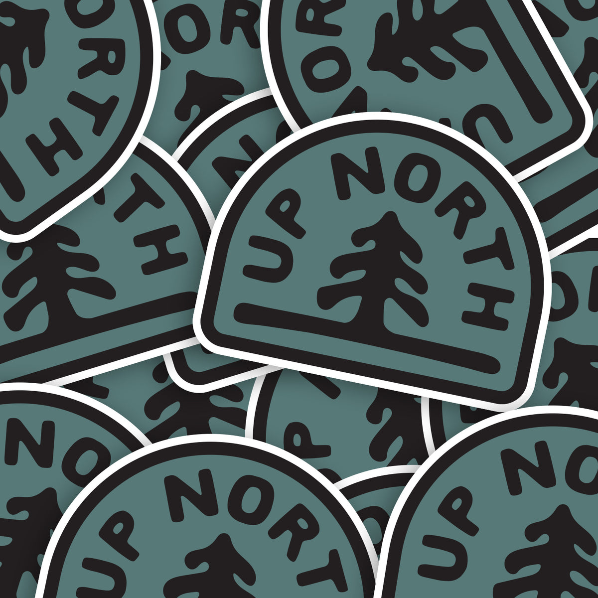 A loose pile of Up North stickers overlaps, each teal badge showing the same pine and lettering.