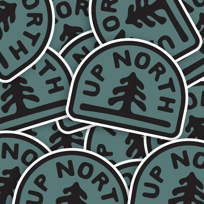 A loose pile of Up North stickers overlaps, each teal badge showing the same pine and lettering.