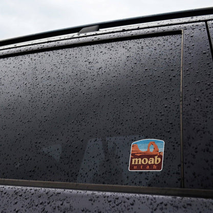 Rain beads across a dark car window where the Moab Utah sticker holds its place near the door frame.