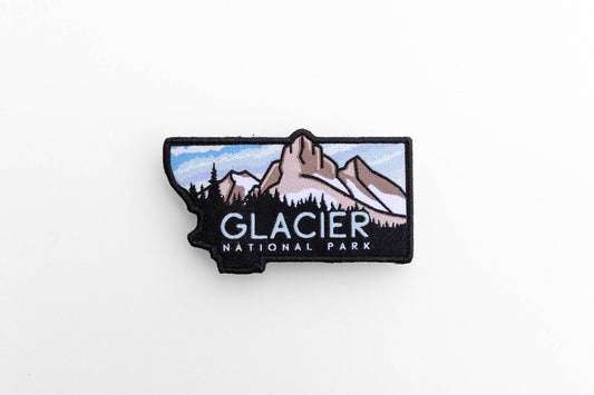 Laid flat on white, the Glacier National Park patch is cut to the shape of Montana with peaks and pines stitched inside.