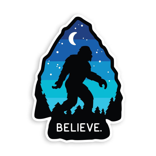 Arrowhead shaped Bigfoot Believe sticker on white, with a striped blue night sky, crescent moon and pines.
