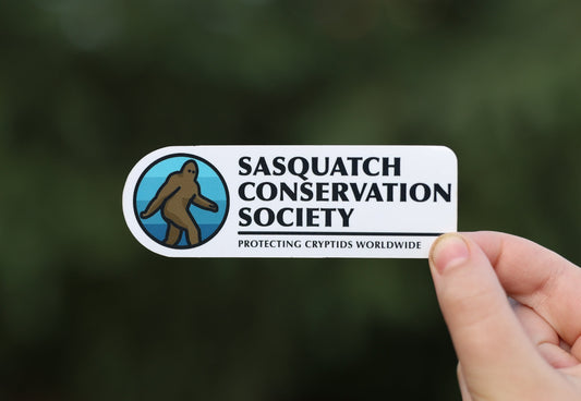 Held further back in soft daylight, the Sasquatch Conservation Society sticker reads Protecting Cryptids Worldwide.