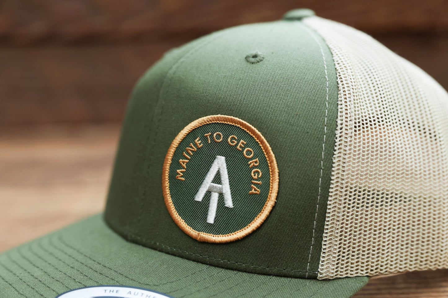 Close on the stitched patch, where the Appalachian Trail trucker hat spells Maine to Georgia in white and gold.