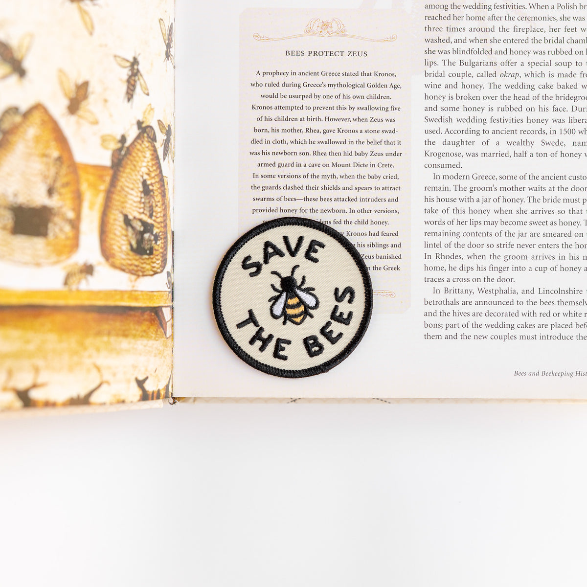The Save The Bees patch sits on an open book page about bees protecting Zeus, its bee stitched in gold and black.