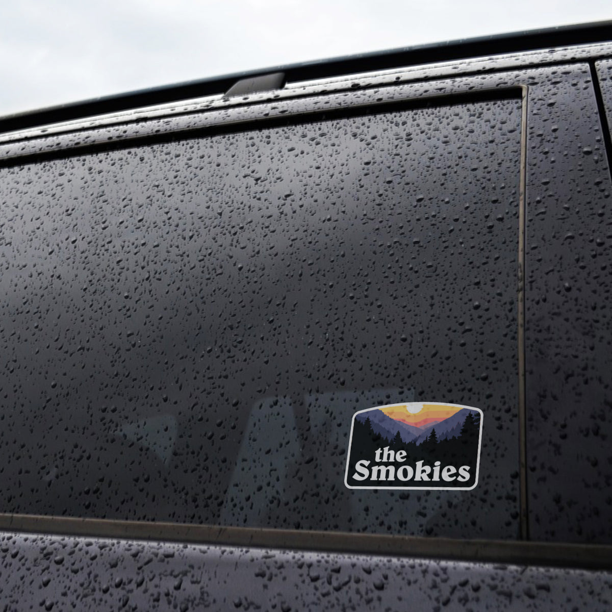 Raindrops cover a dark truck window where the The Smokies sticker sits applied near the frame.