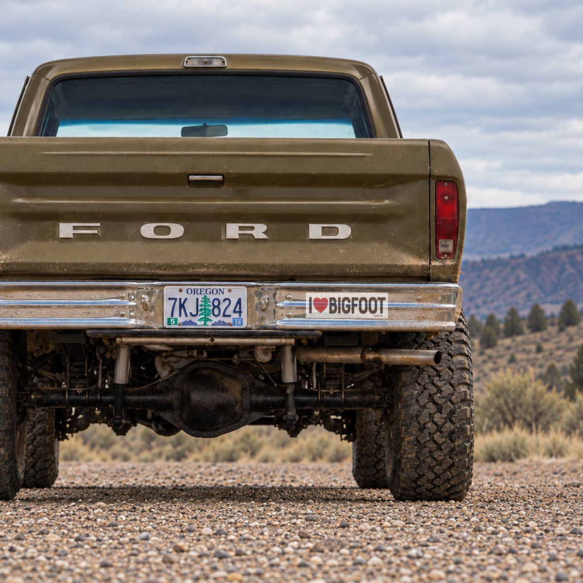 An olive Ford pickup shows the I Heart Bigfoot sticker tucked beside its Oregon plate above rugged tires.