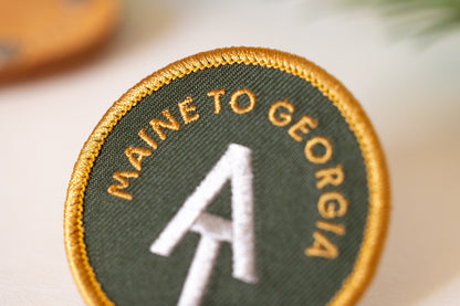 Close crop on the AT Maine to Georgia patch, where gold letters curve above the white trail monogram.