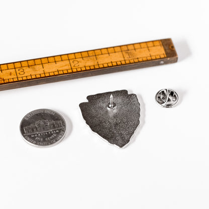 Turned face down beside a ruler and a nickel for scale, the Leave No Trace pin reveals its post and butterfly clasp.