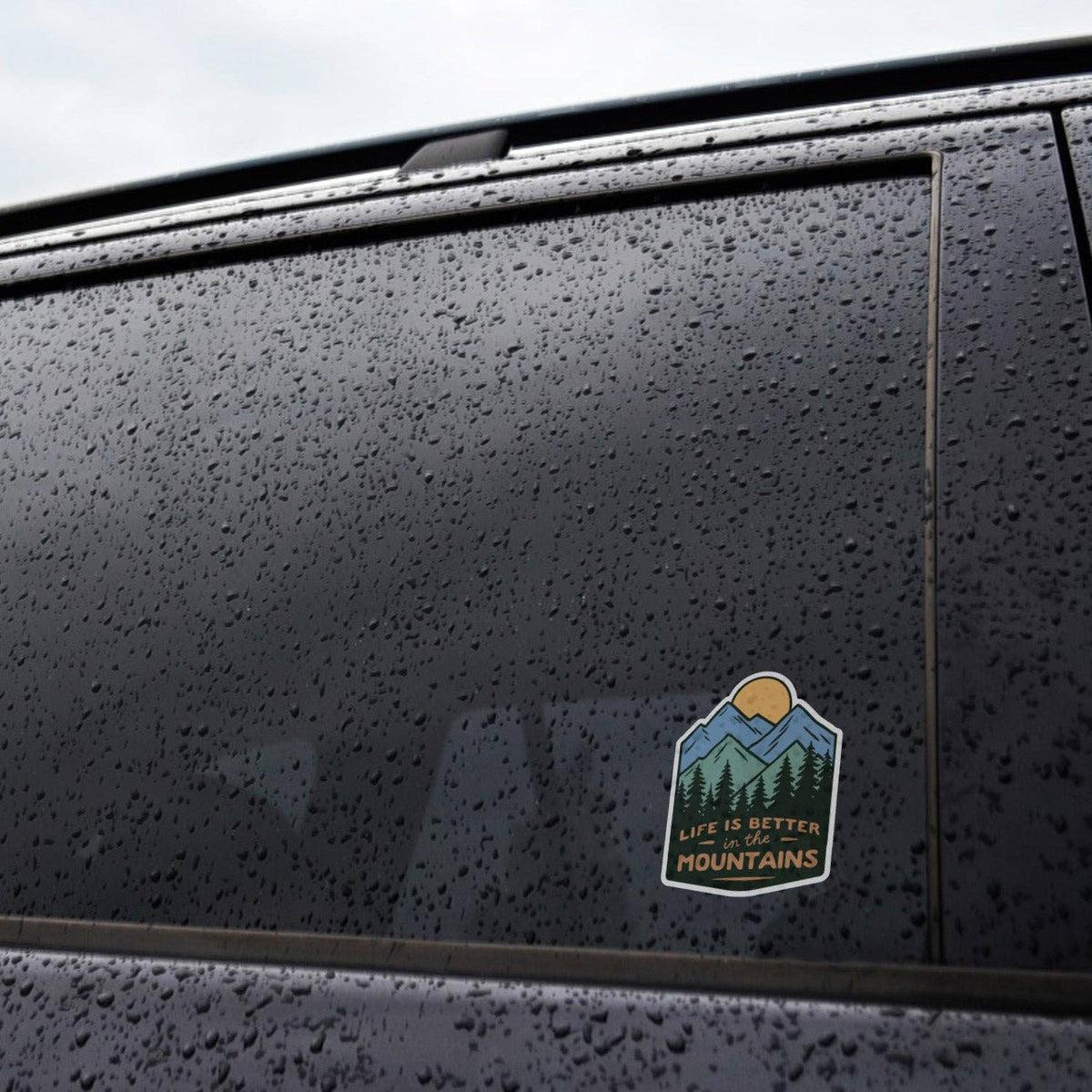 Applied to the rain speckled window of a dark car, the Life Is Better In The Mountains sticker stays put.