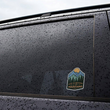 Applied to the rain speckled window of a dark car, the Life Is Better In The Mountains sticker stays put.