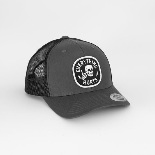 Against a plain white background, the grey Everything Hurts trucker hat shows its black mesh back and skull patch.