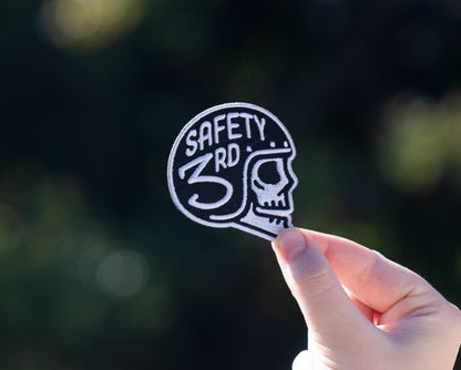 Held a little farther back in sunlight, the Safety 3rd Helmet Patch reads clearly against dark foliage.