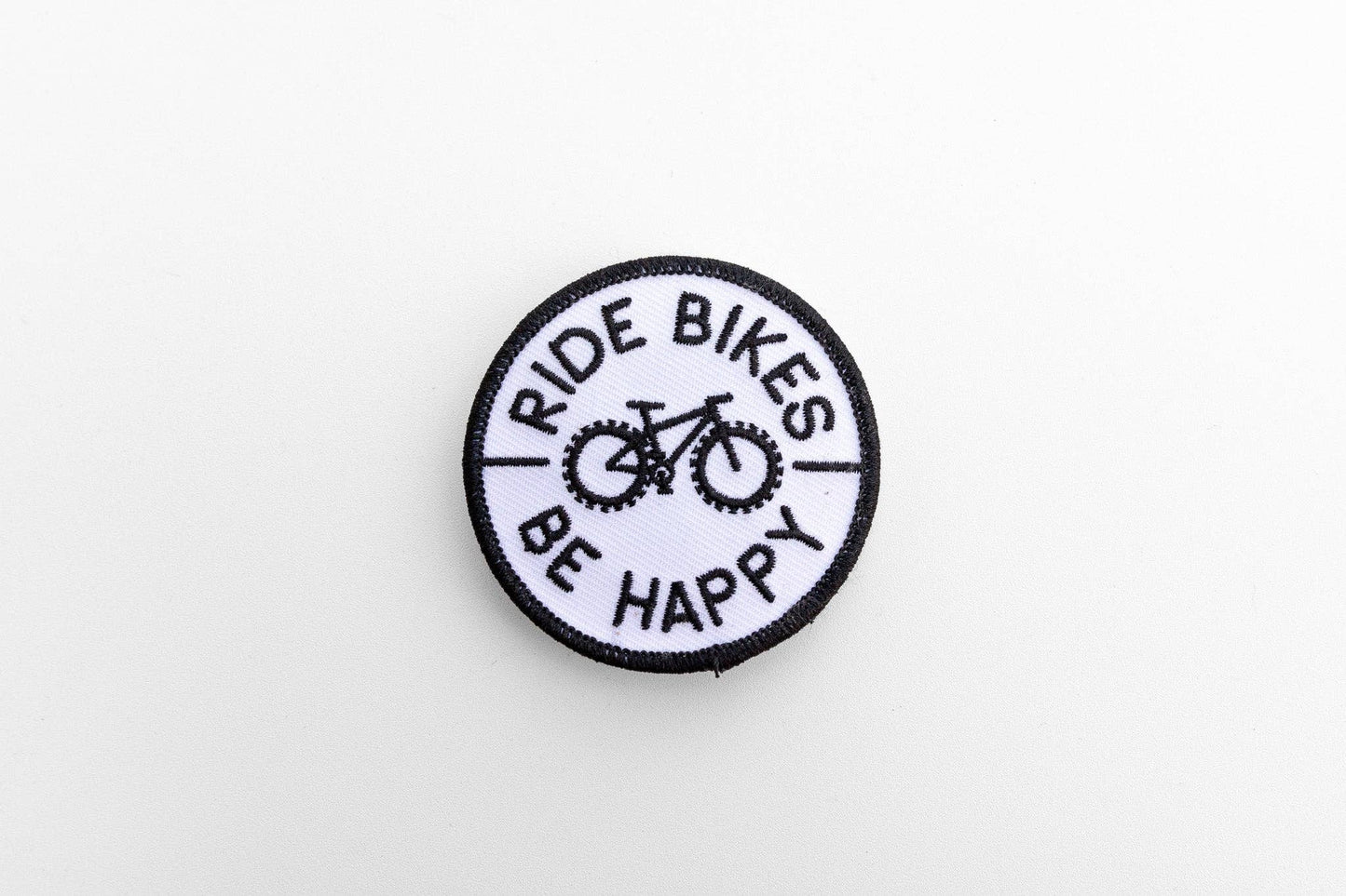 On a plain white background, the round Ride Bikes Be Happy patch shows its black bicycle and border stitching.