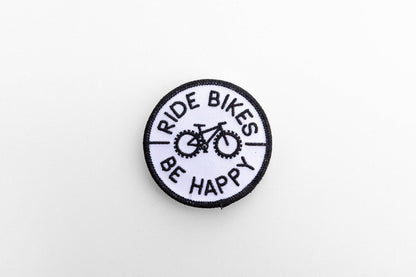 On a plain white background, the round Ride Bikes Be Happy patch shows its black bicycle and border stitching.