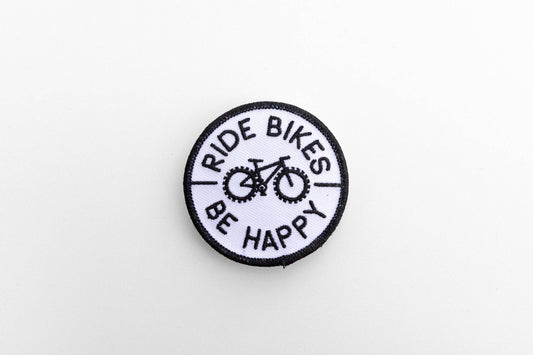 On a plain white background, the round Ride Bikes Be Happy patch shows its black bicycle and border stitching.