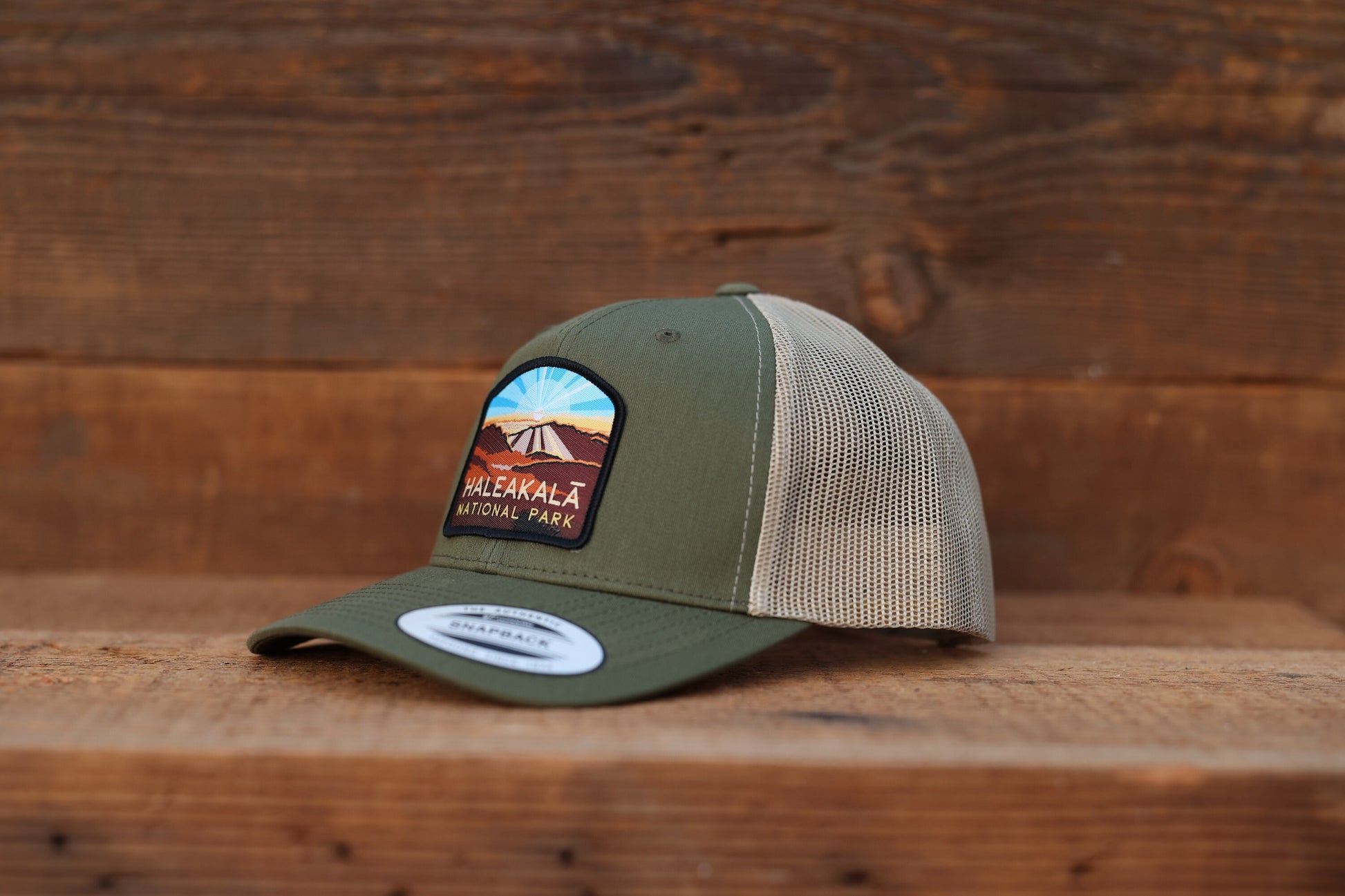 Resting on a wooden bench, the Haleakala National Park trucker hat faces left with a snapback label on the brim.