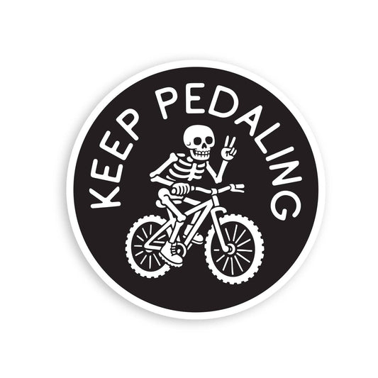 Round black Keep Pedaling MTB sticker on white, a skeleton throwing a peace sign while riding a mountain bike.