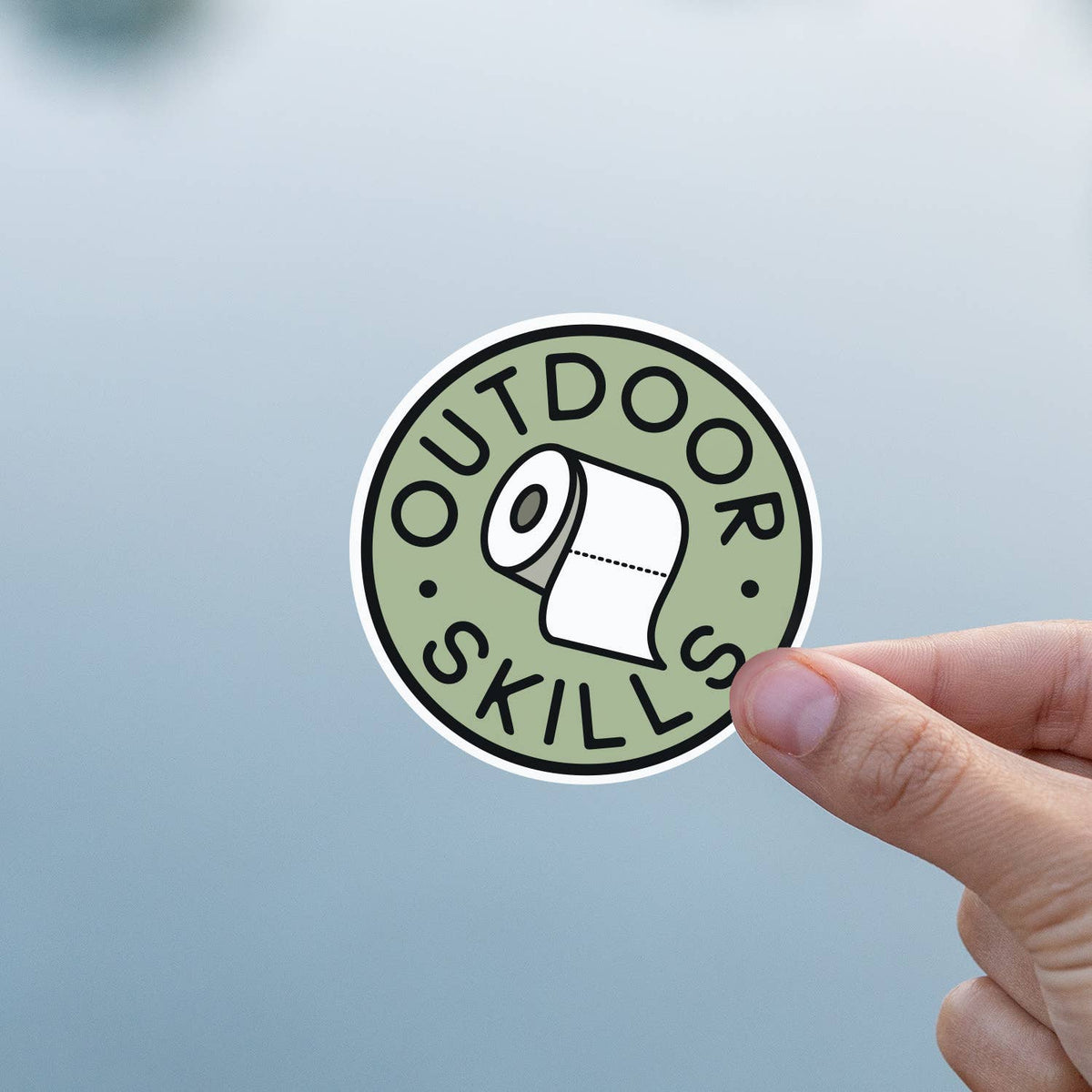 Close and sharp, the Outdoor Skills sticker is held against a soft grey blue background.