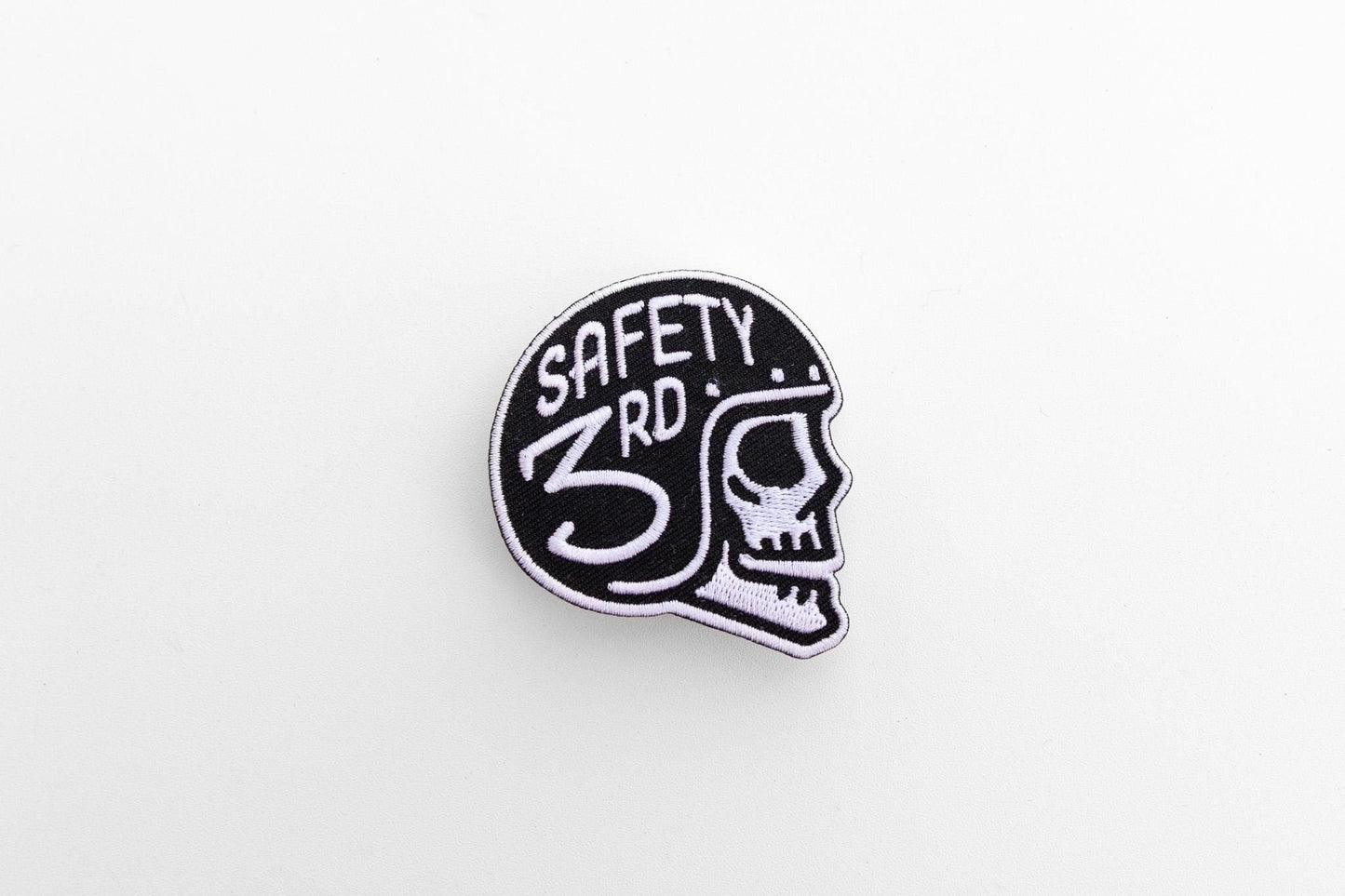 Small against a wide white background, the Safety 3rd Helmet Patch sits alone with its skull facing right.